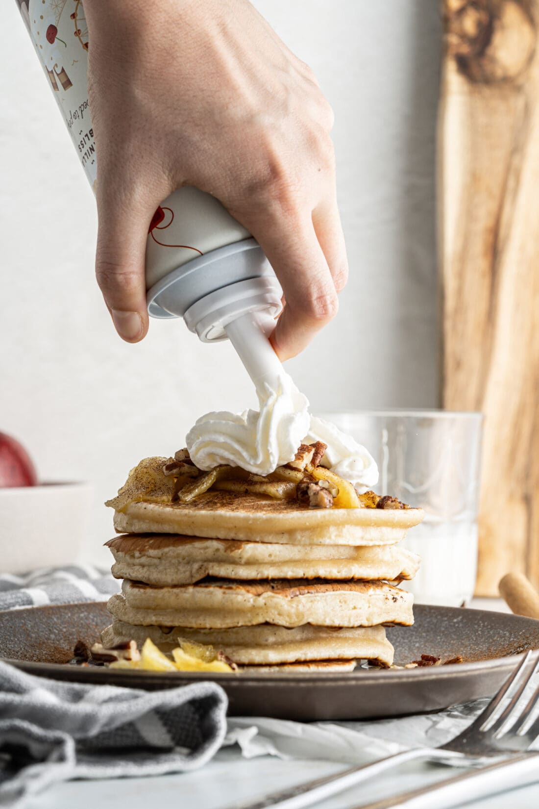 adding whipped cream to a stack of Apple Pancakes
