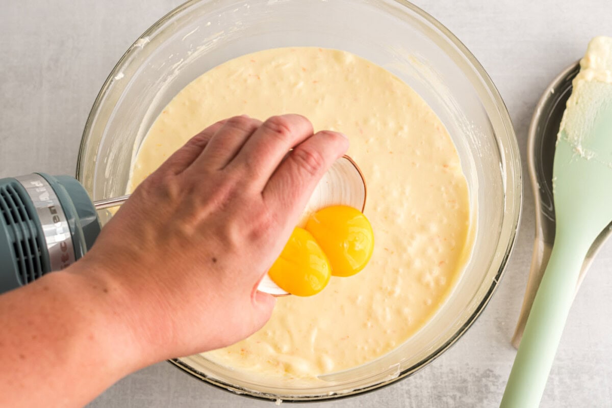 hand pouring egg yolks into pound cake batter