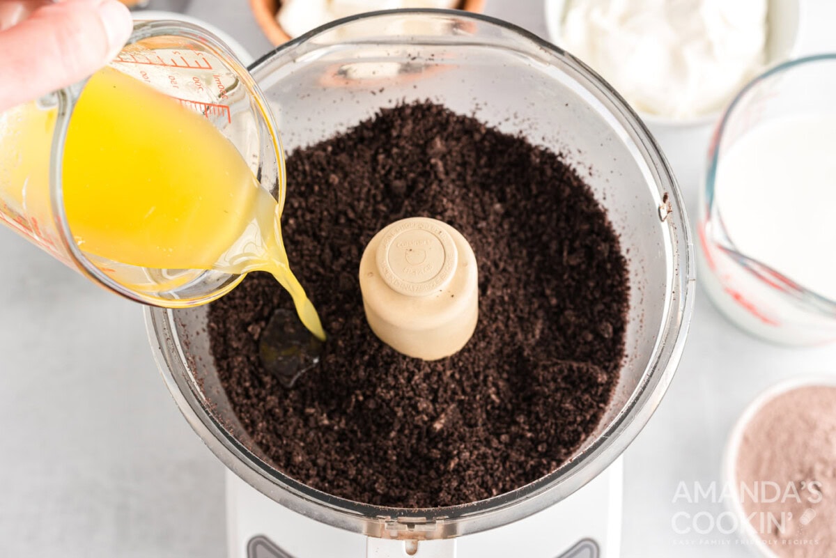 pouring melted butter into oreos crumb in a food processor