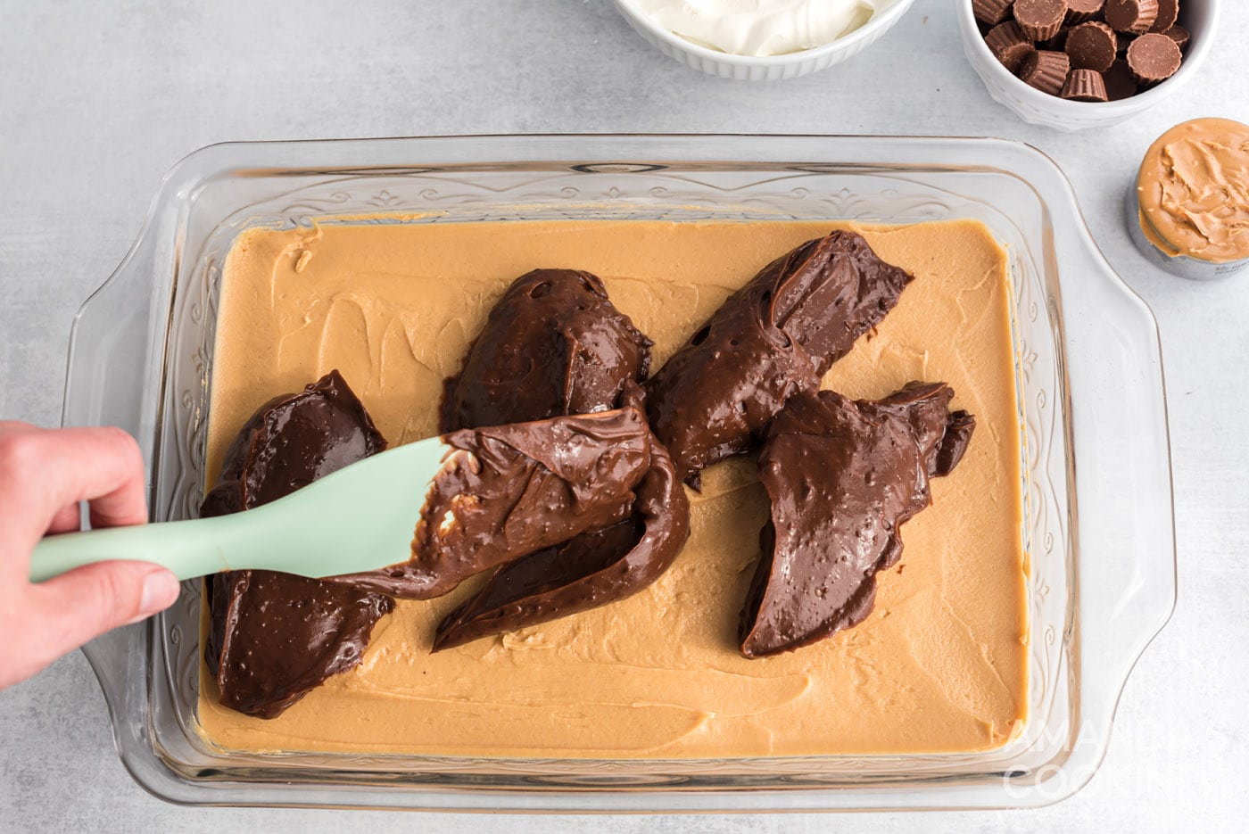 rubber spatula spreading chocolate pudding over peanut butter