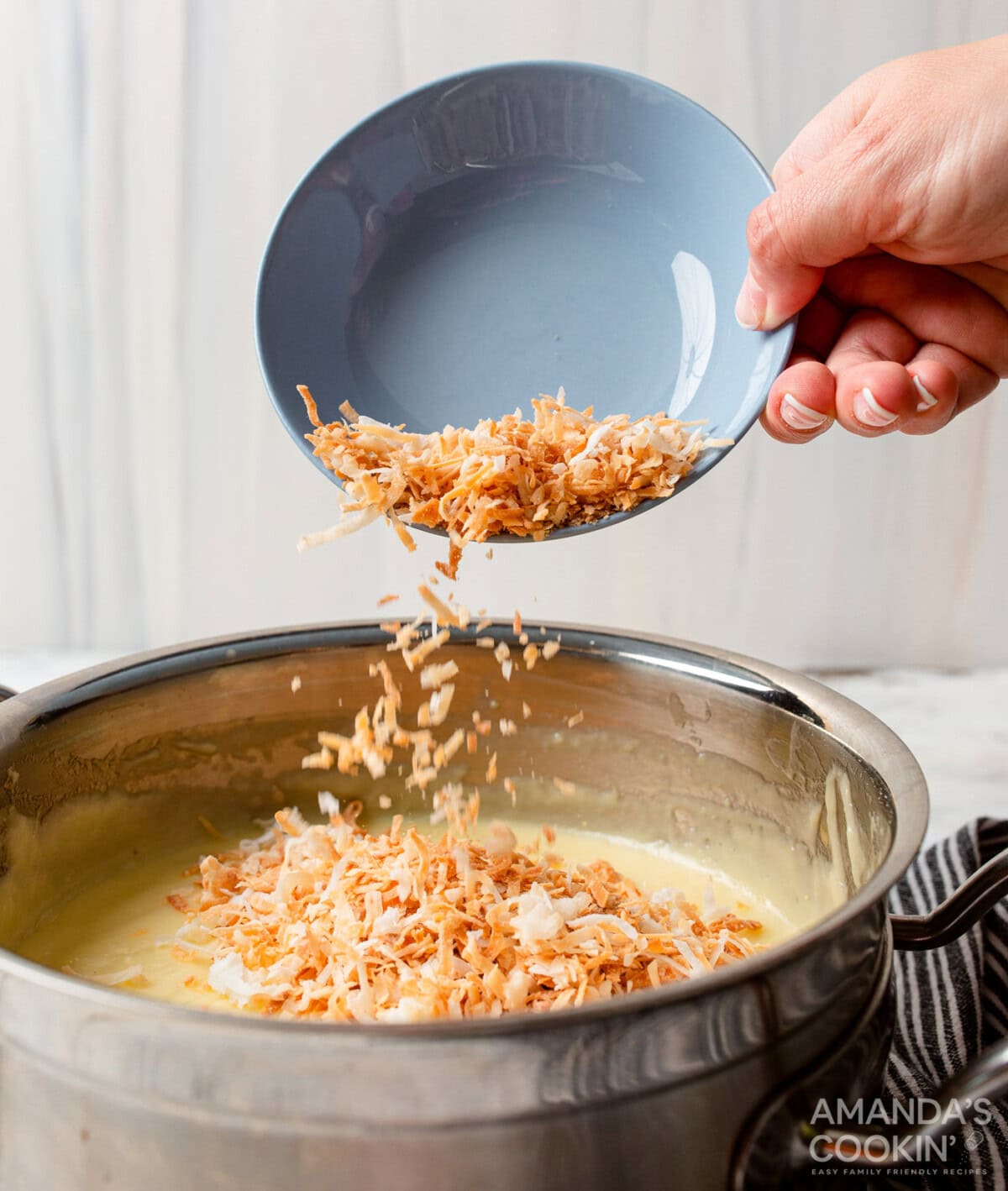 adding shredded coconut to coconut custard in a saucepan