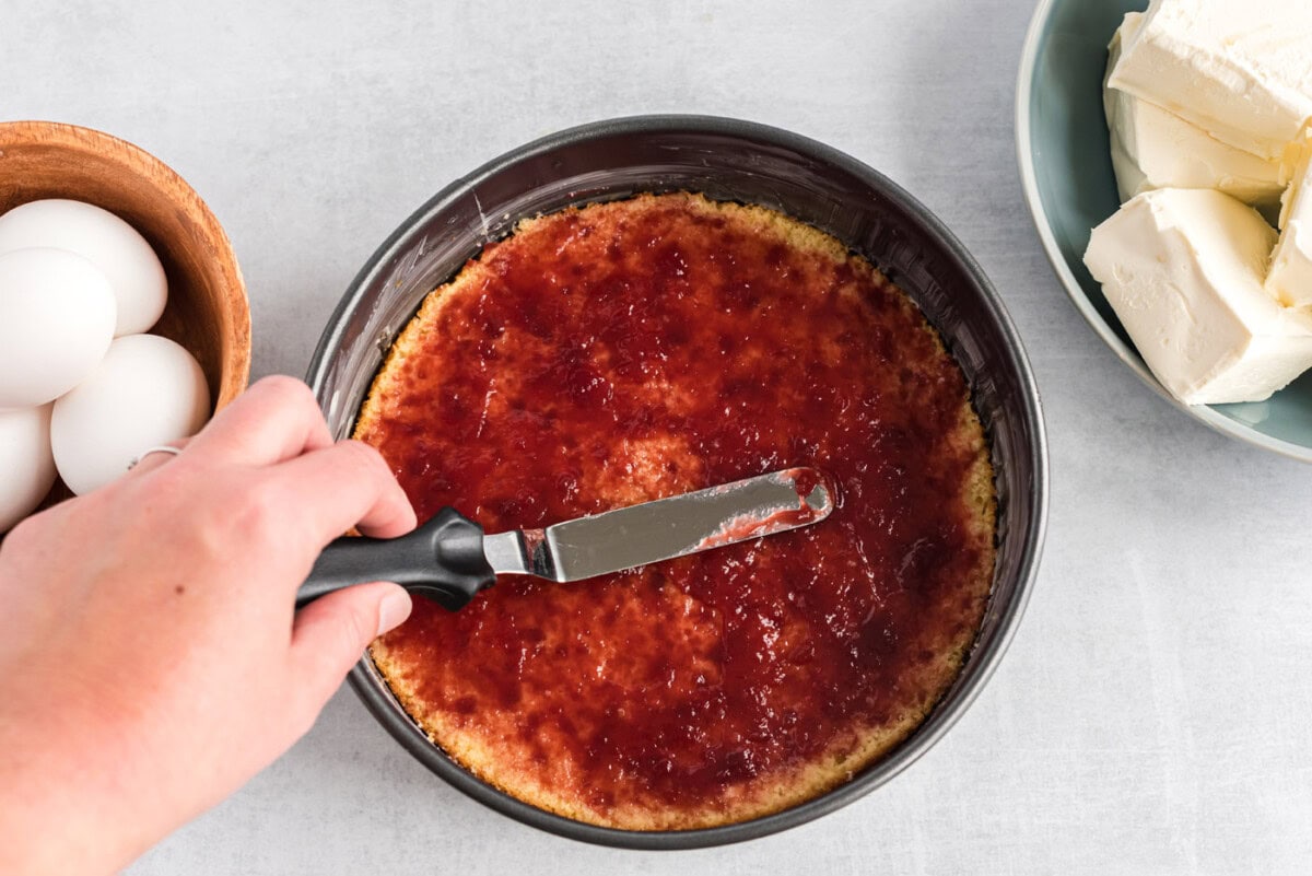 spreading raspberry preserves on top of yellow cake