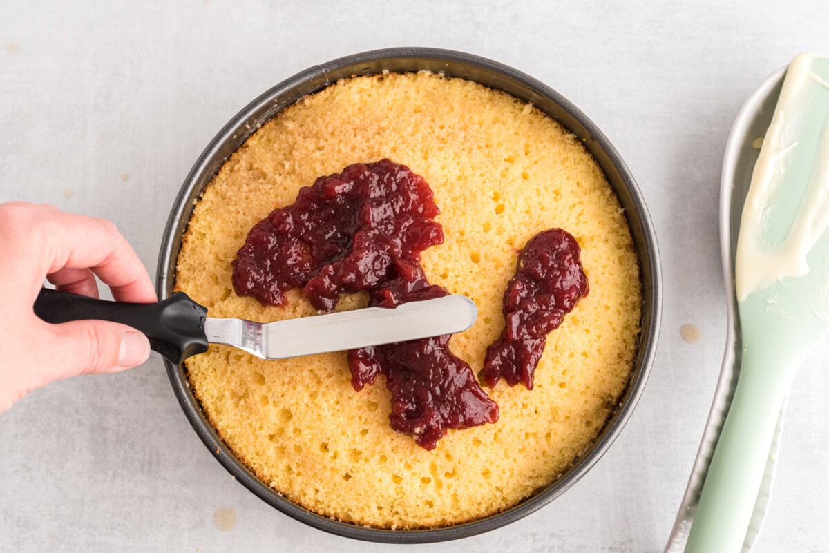 icing spatula spreading raspberry preserves over cake