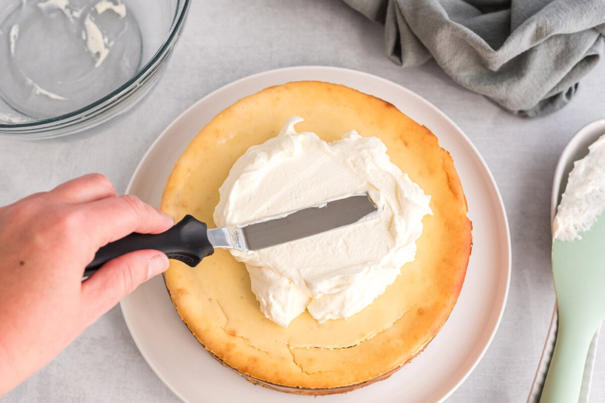 icing spatula spreading whipped cream on top of cheesecake