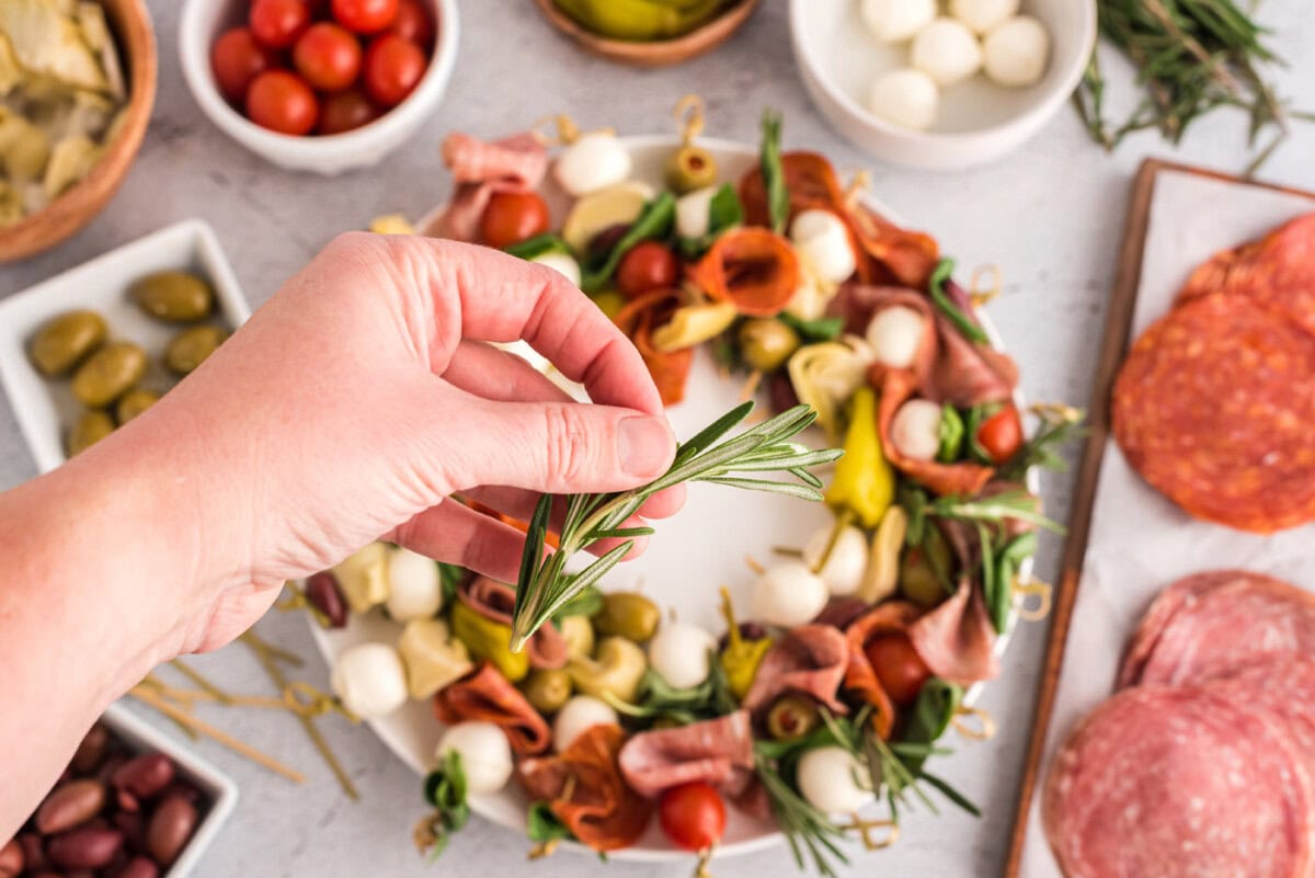 hand holding rosemary sprig over antipasto wreath