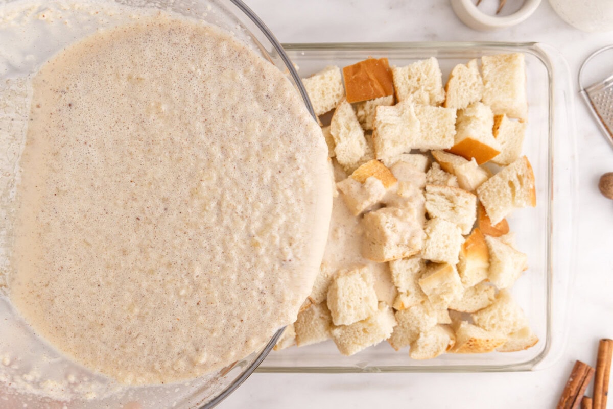 pouring cream mixture over bread cubes in a baking dish