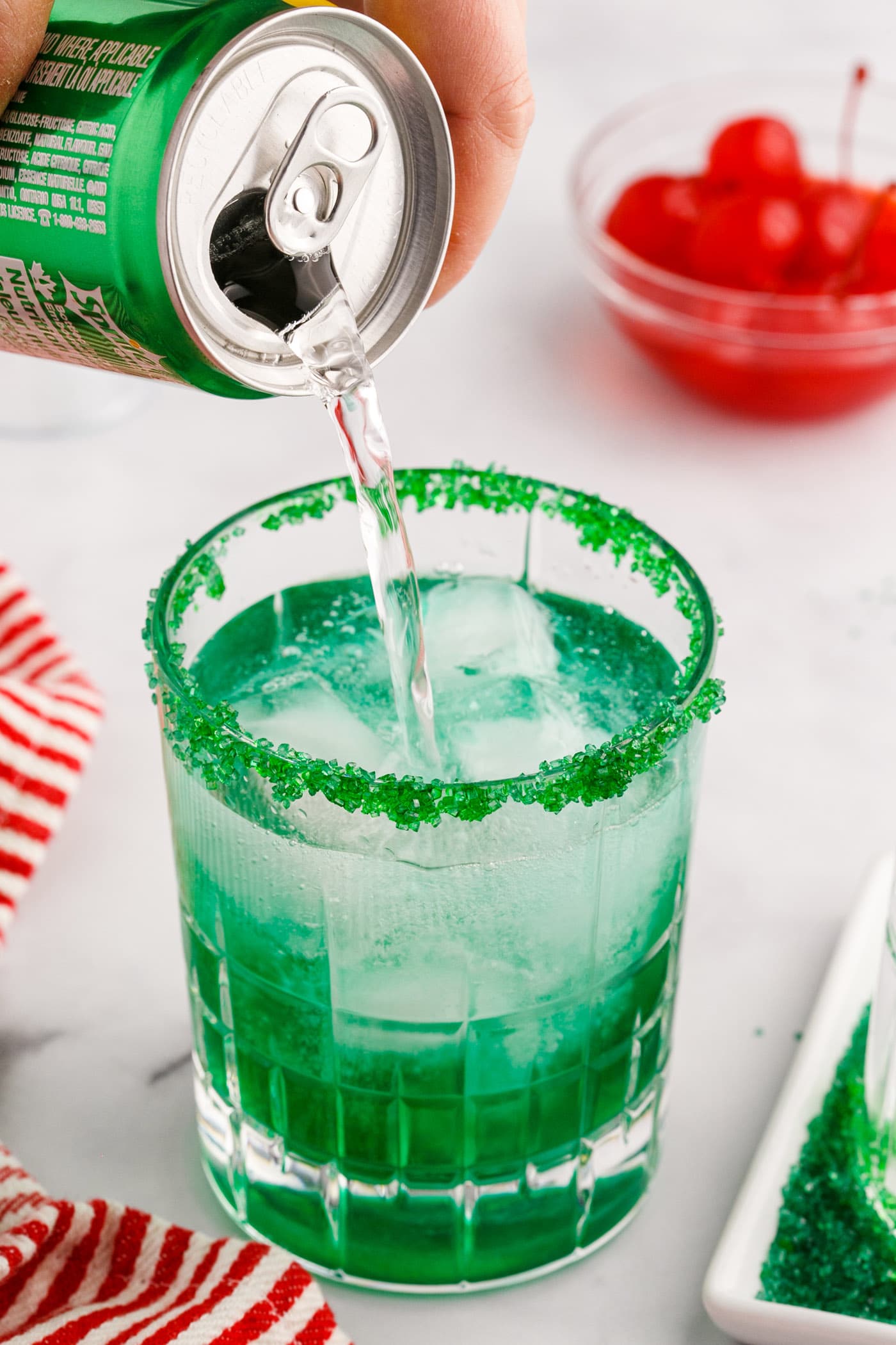 pouring lemon lime soda into grinch cocktail with sugared rim