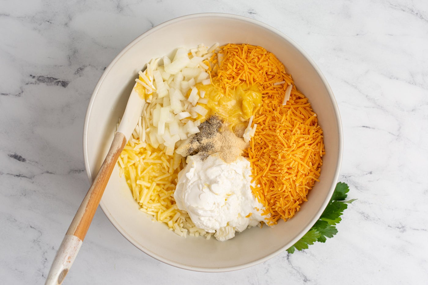 cheese, hashbrowns, sour cream, and cream of chicken soup with seasonings in a mixing bowl