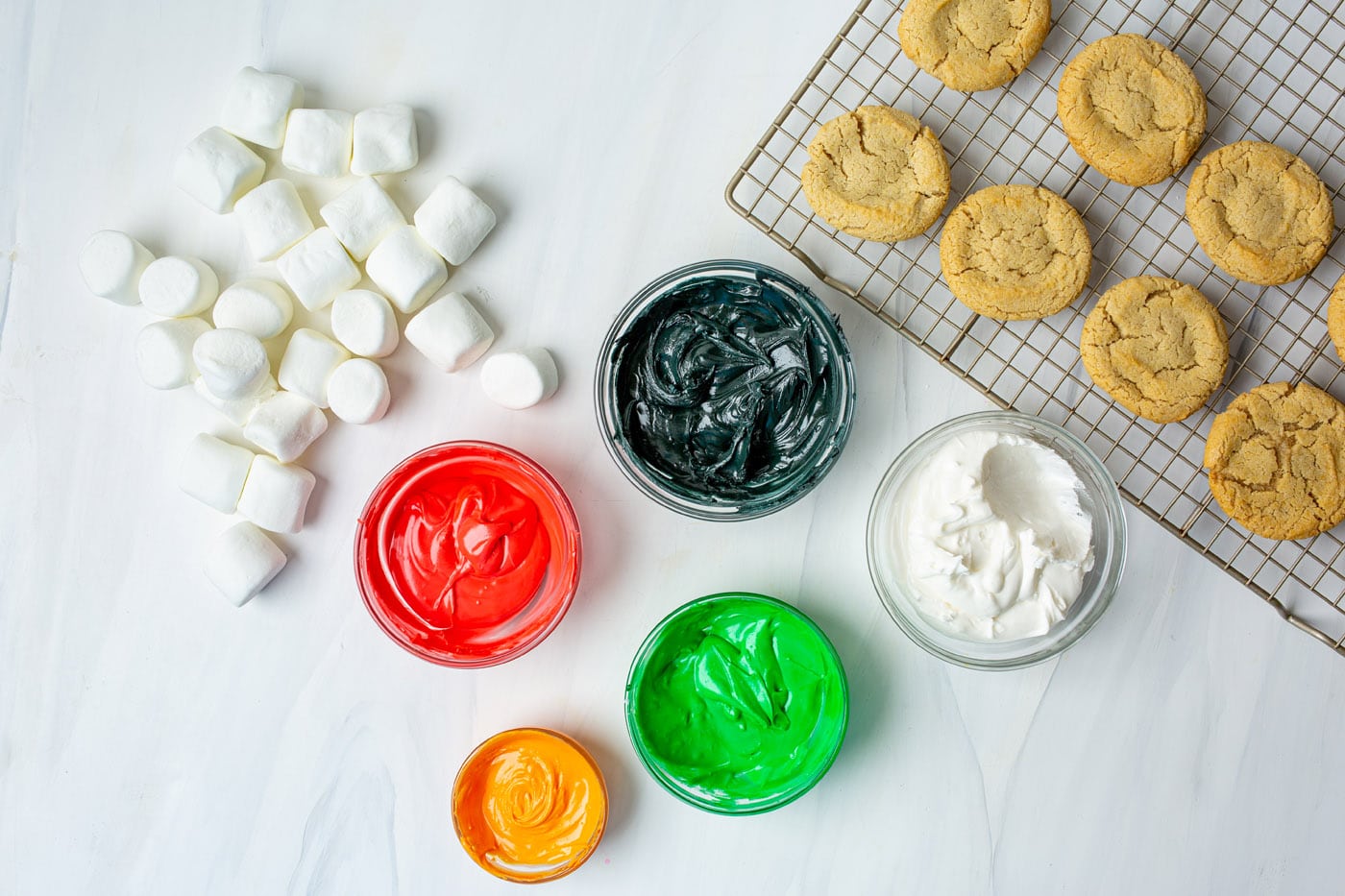 colorful icing in bowls with marshmallows and cookies