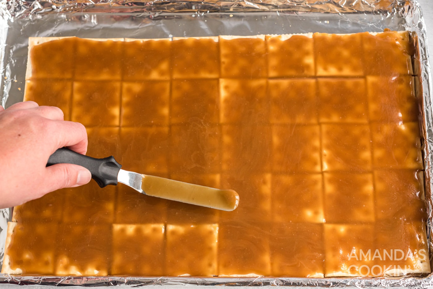 spatula spreading caramel over saltine crackers