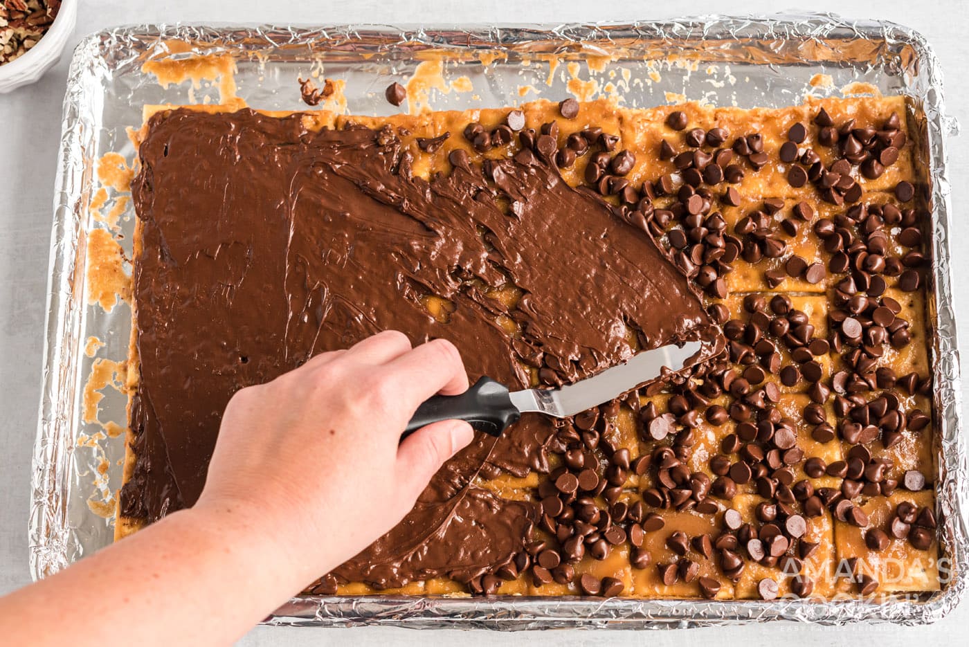 spatula spreading melted chocolate over saltine toffee