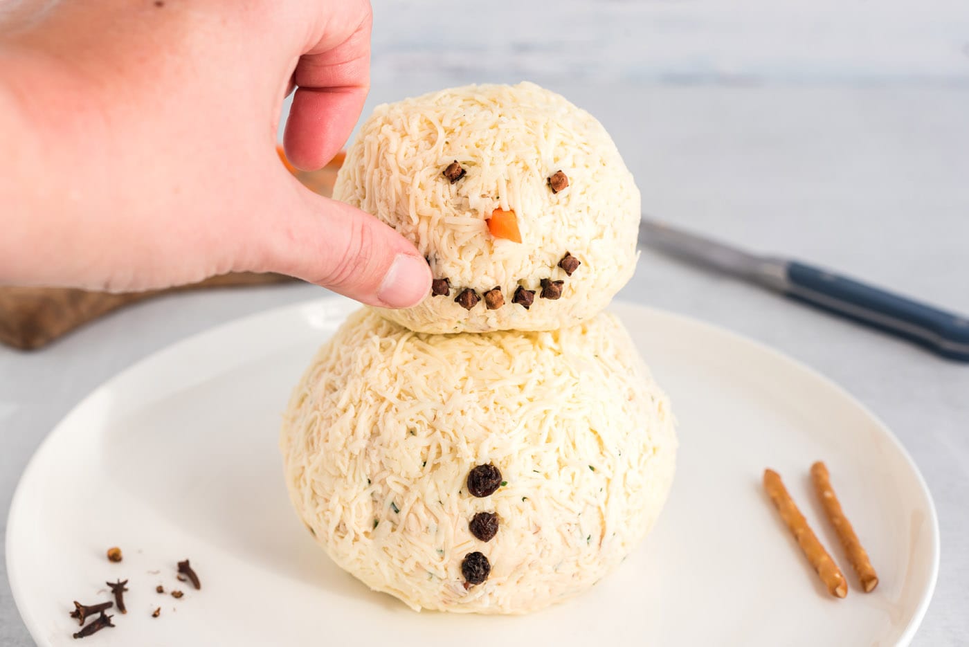 hand pressing cloves into snowman cheeseball