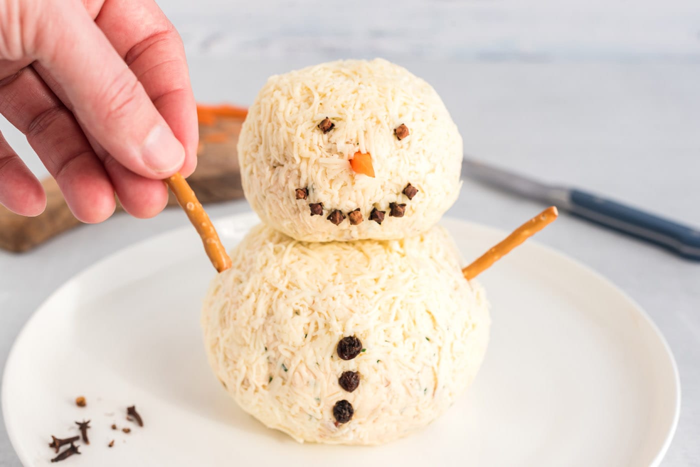 hand adding a pretzel stick to snowman cheeseball