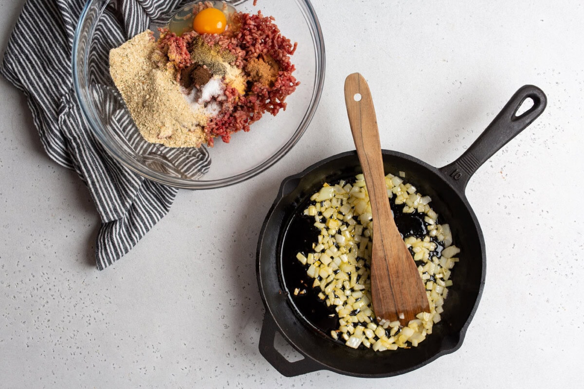 meatball ingredients in a mixing bowl with sauteed onions in a skillet