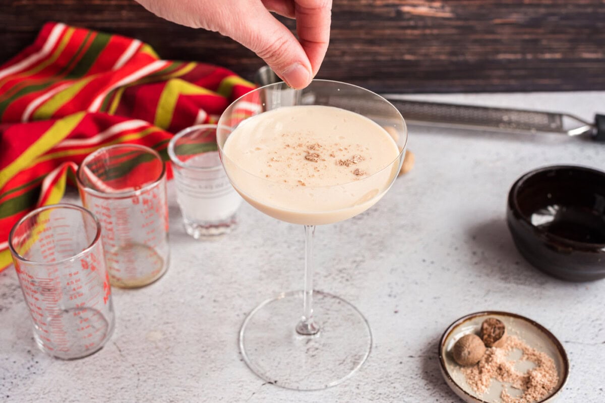 hand sprinkling ground nutmeg on top of brandy alexander cocktail