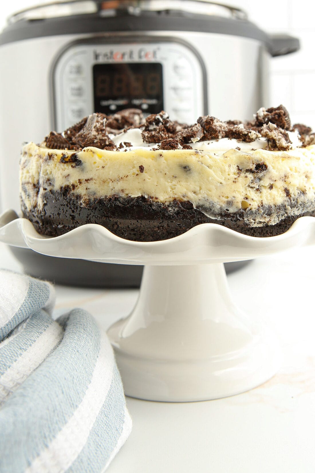 Instant Pot Oreo Cheesecake on a cake plate with IP in background