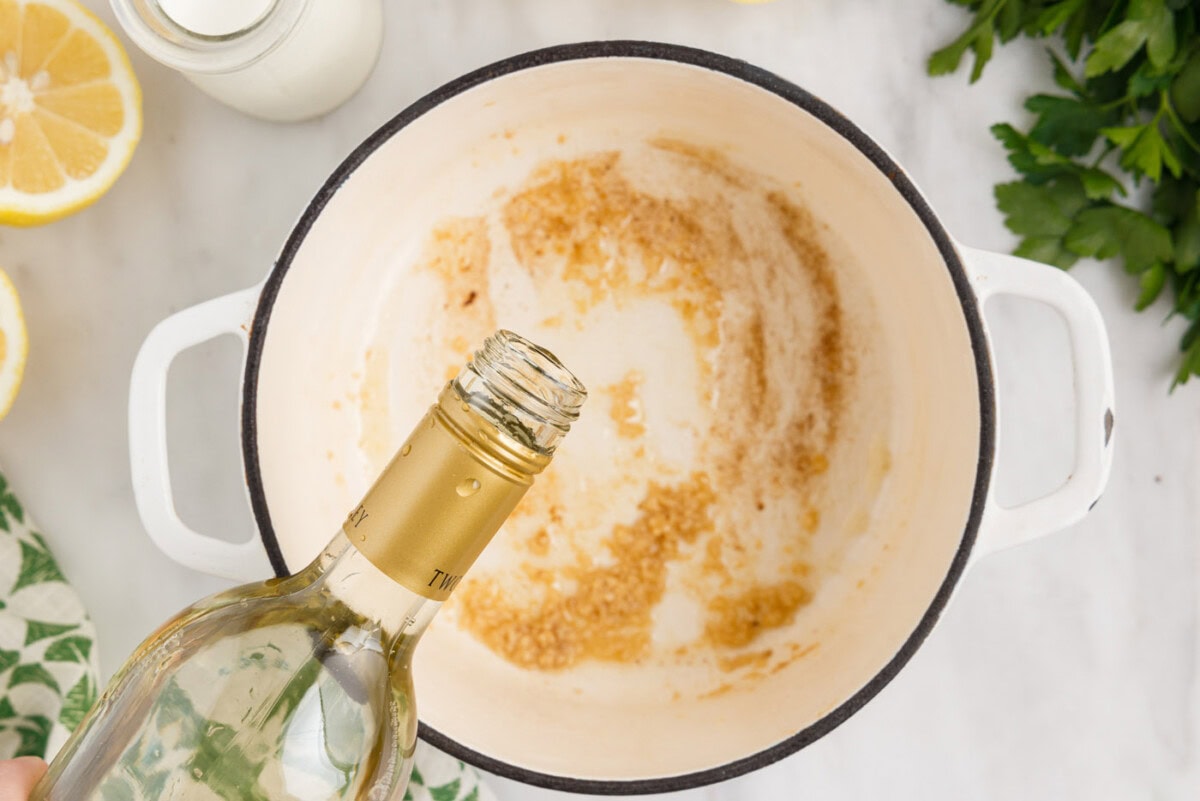 pouring wine into saucepan with garlic and butter