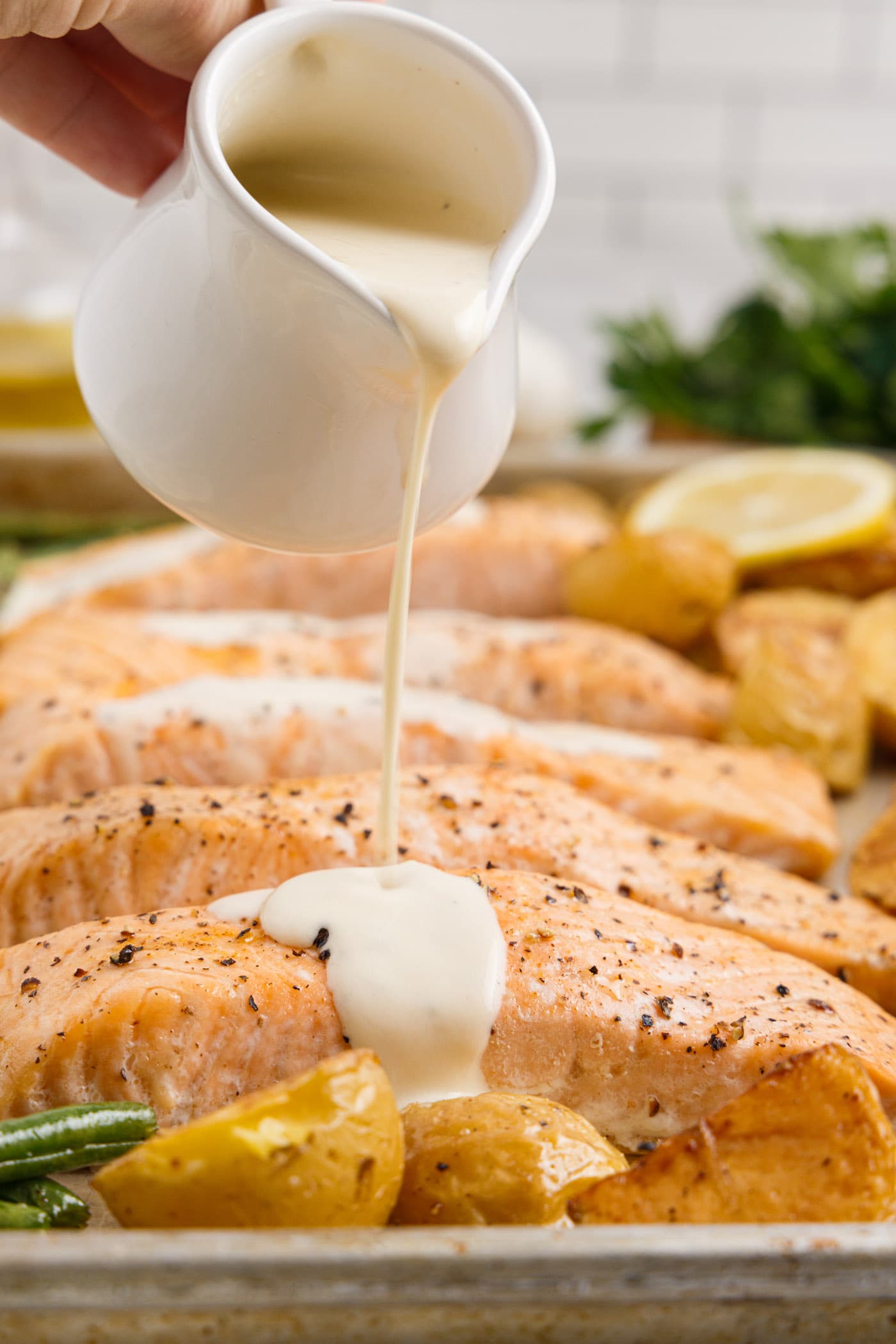 pouring lemon cream sauce on top of baked salmon filets