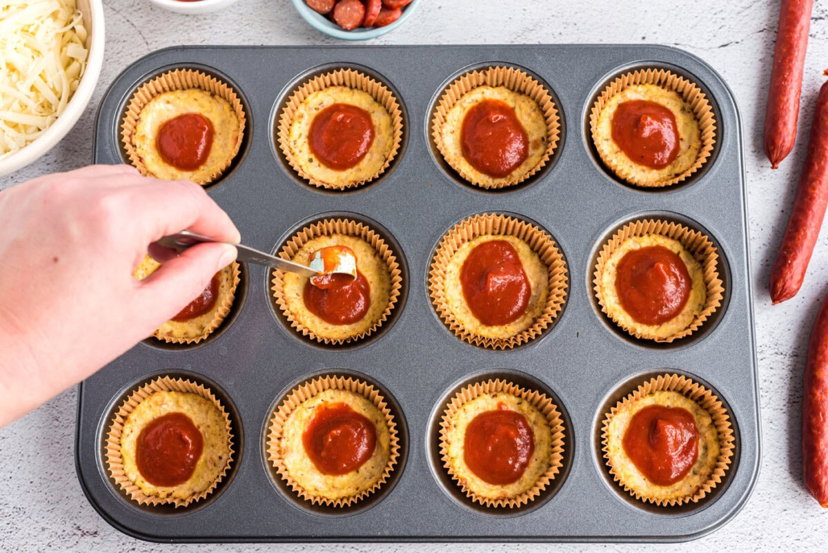 spooning pizza sauce on top of cauliflower pizza bites