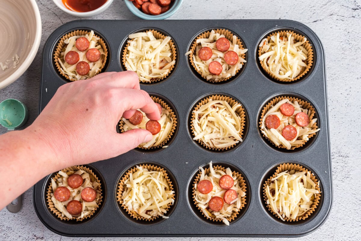 hand adding mini pepperoni to pizza bites