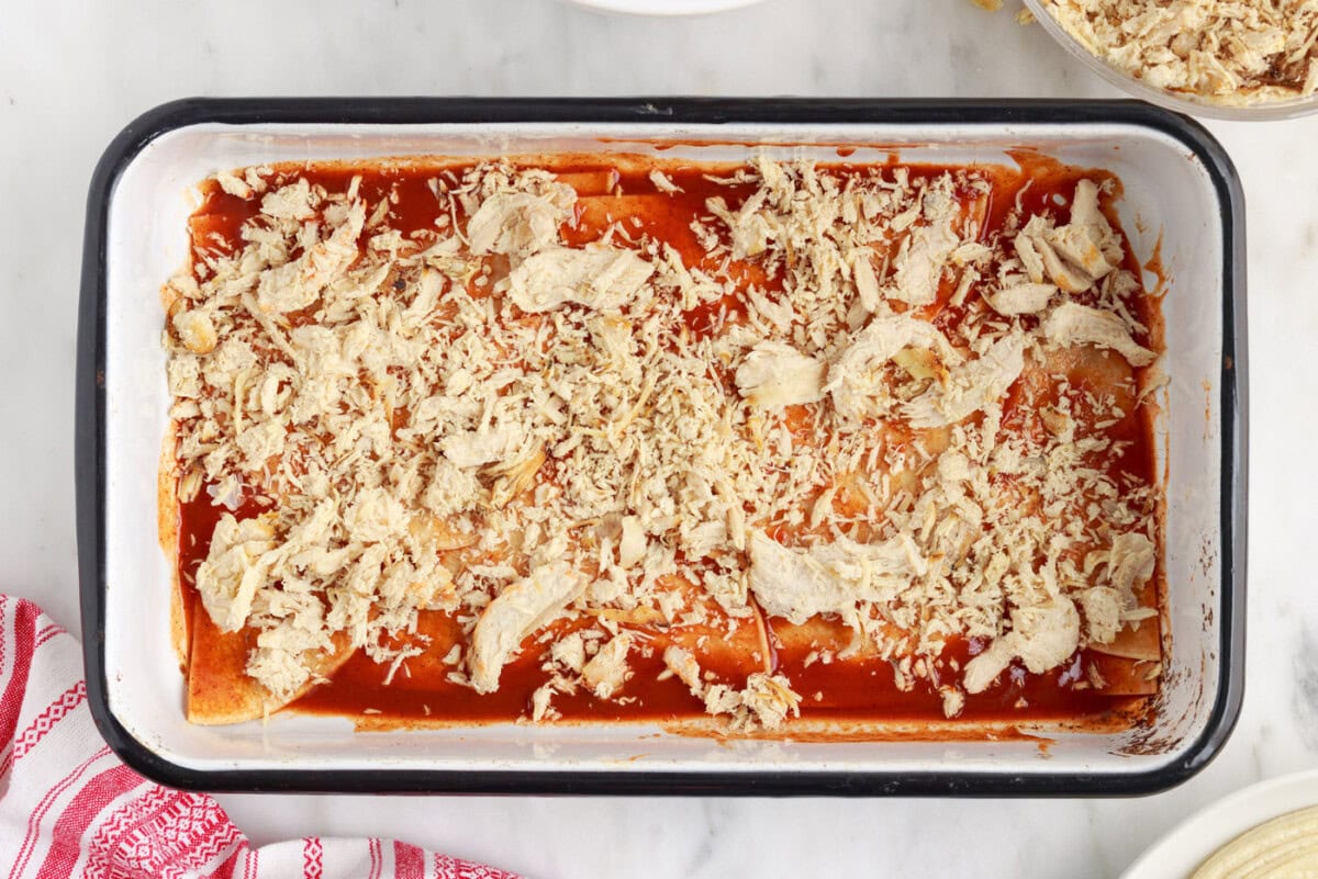 shredded chicken on top of tortillas and enchilada sauce