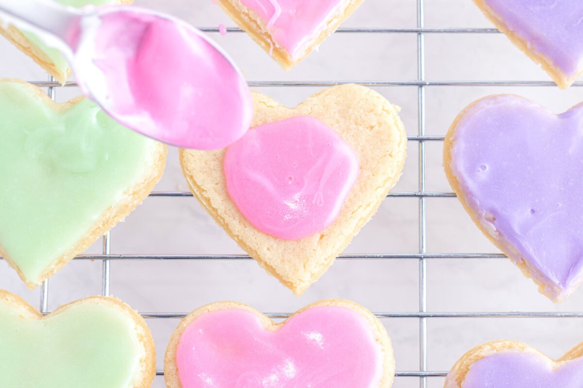 spoon dolloping pink frosting onto sugar cookie