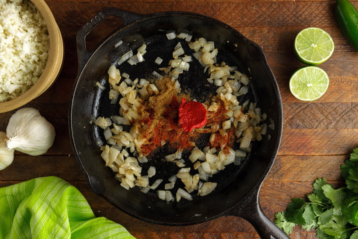 tomato paste and spices added to onion and garlic in a skillet