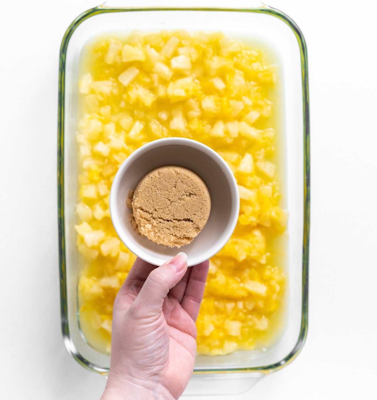 hand holding brown sugar over crushed pineapple in a baking dish