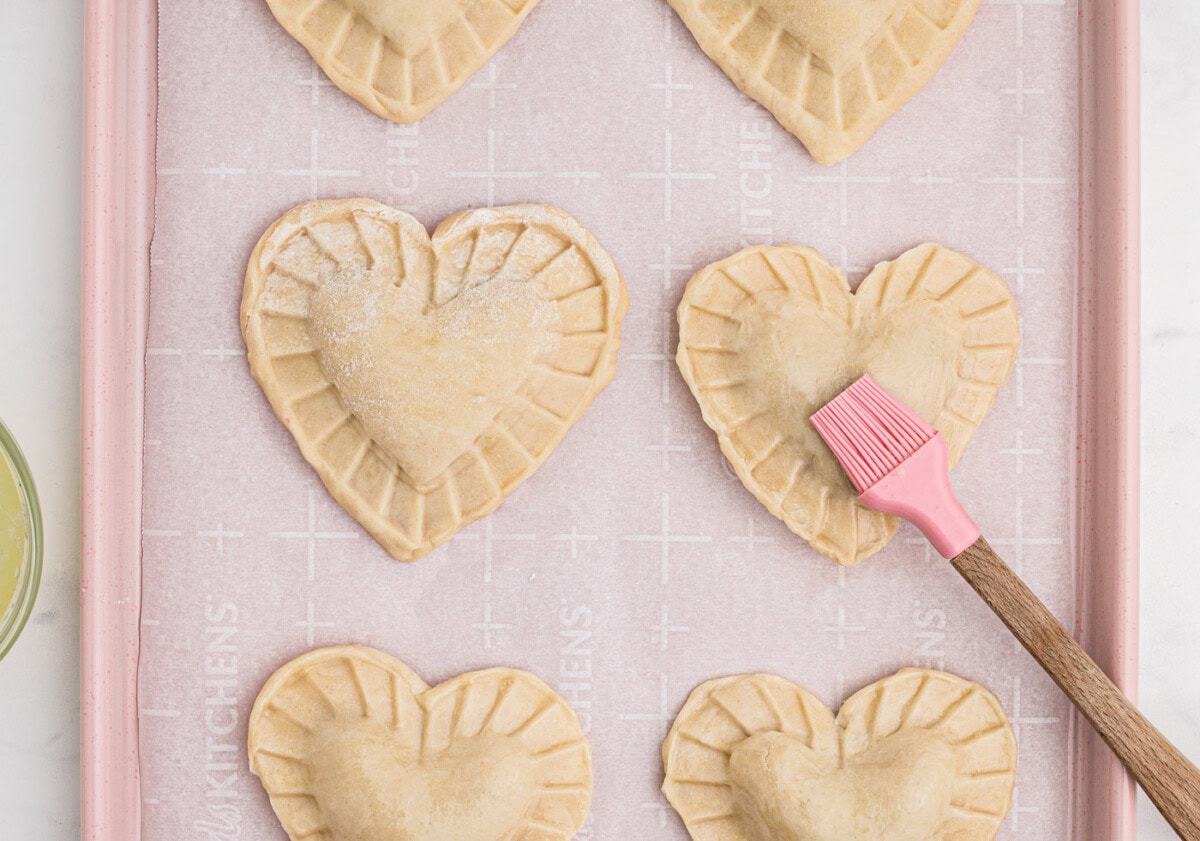 brushing egg wash over heart shaped cherry hand pies