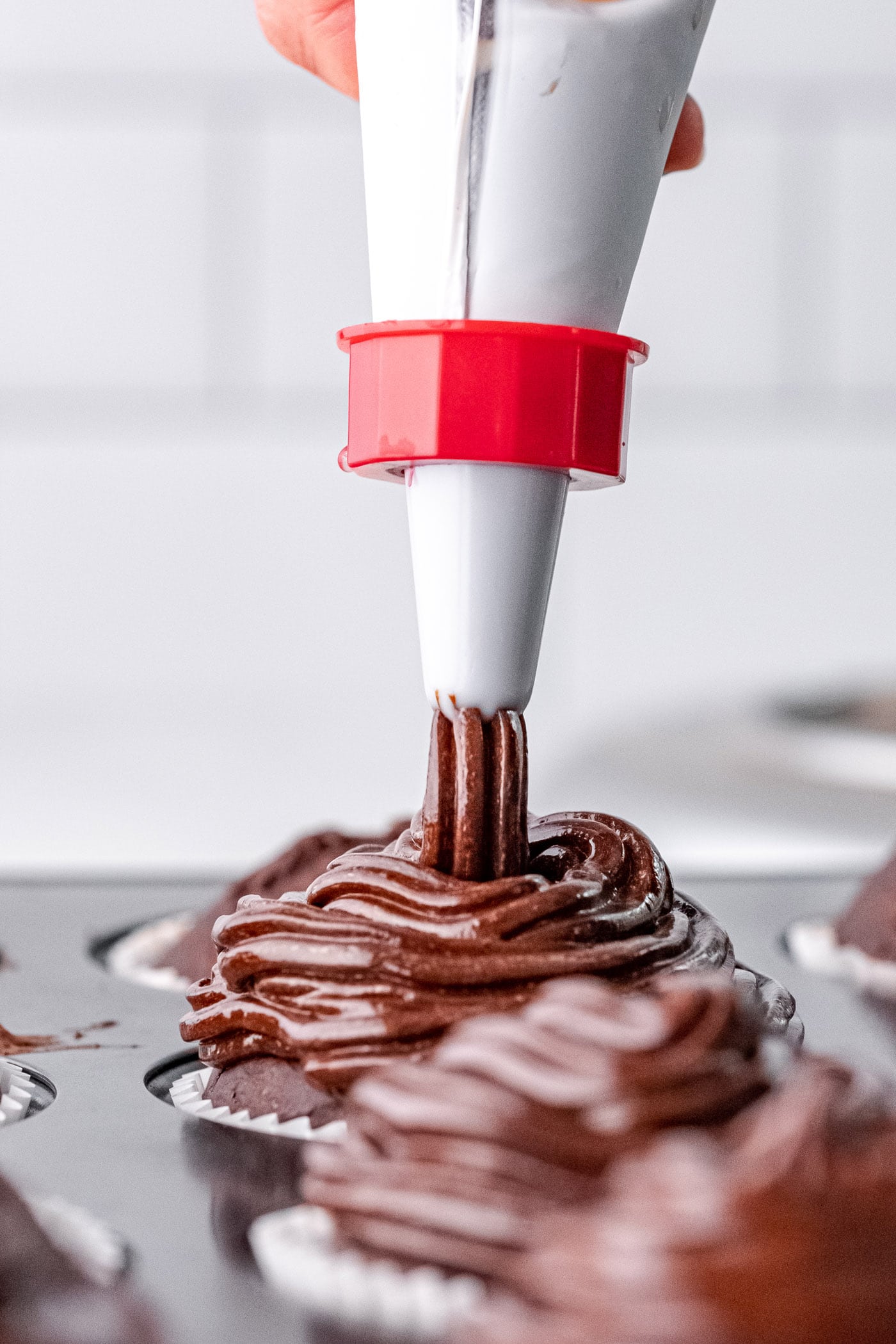 piping chocolate frosting onto cupcakes