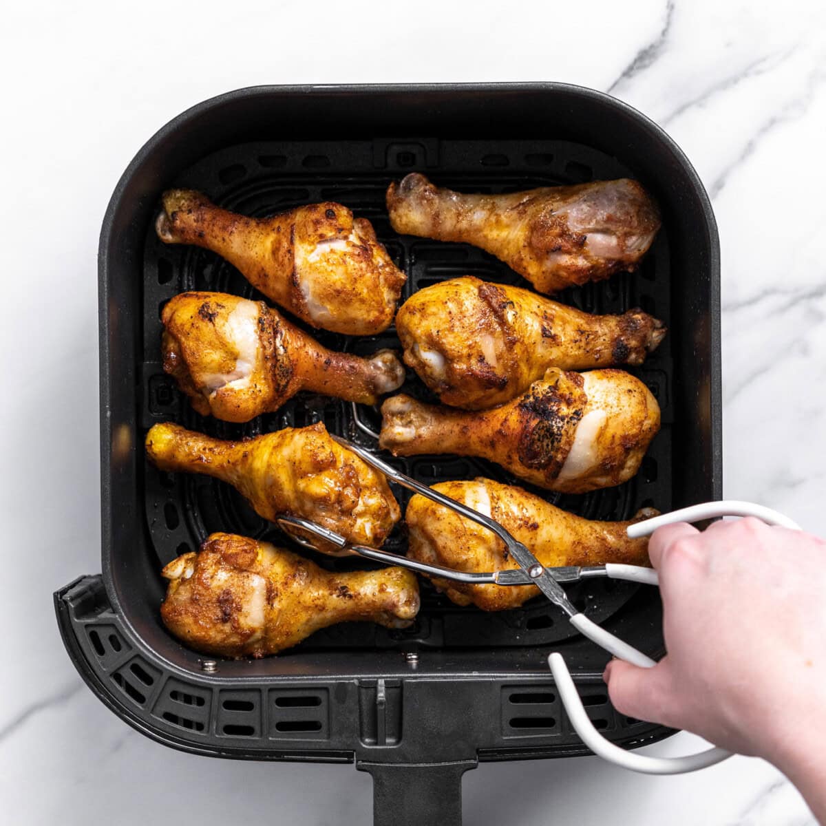 grabbing chicken drumstick in air fryer basket