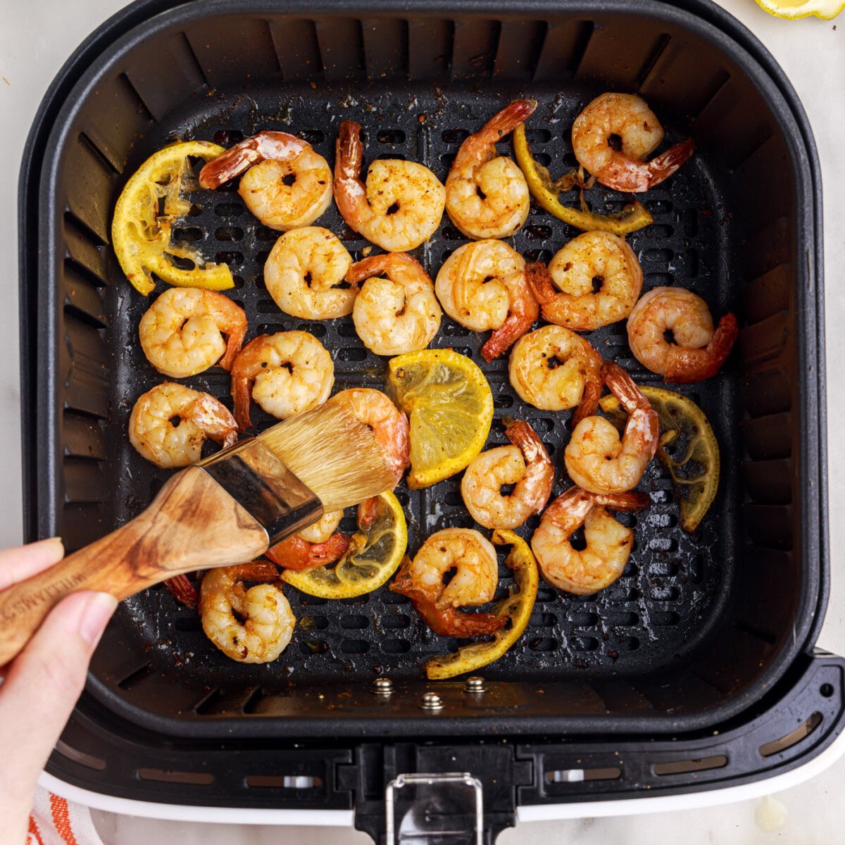 brushing melted butter onto shrimp in air fryer basket