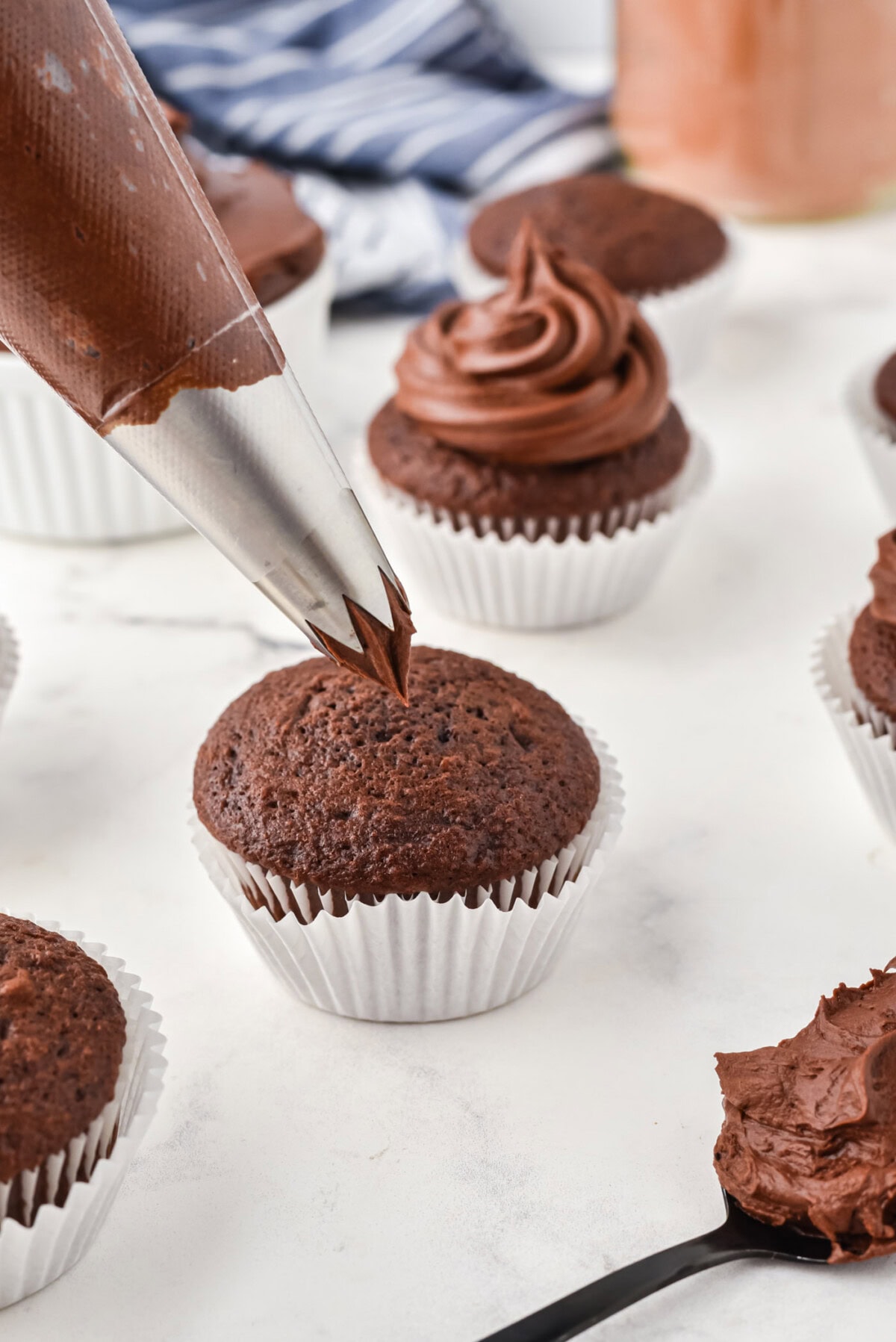 piping Chocolate Fudge Frosting onto cupcake
