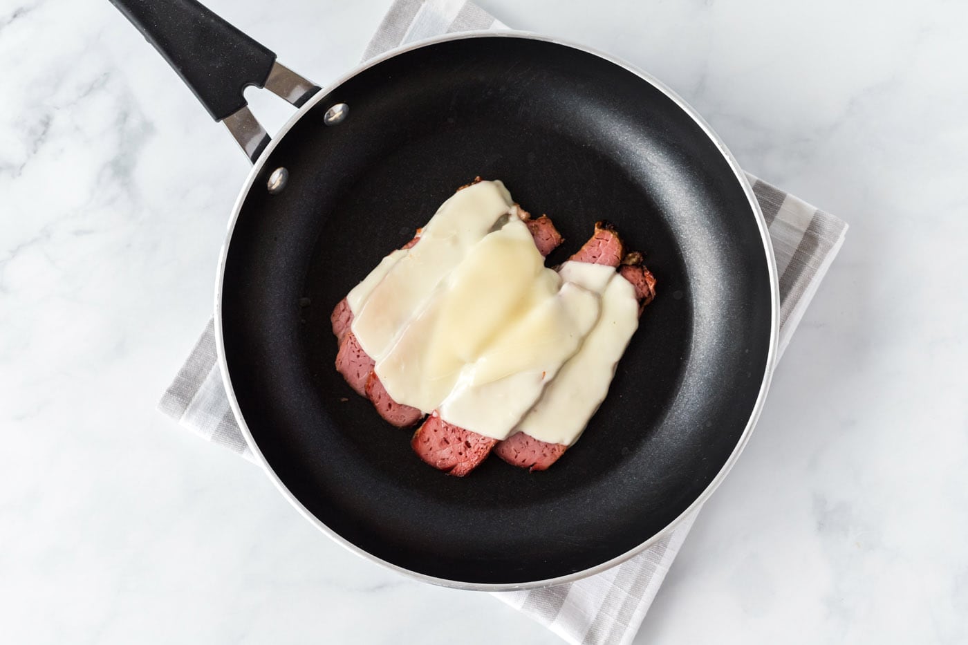 sliced corned beef with mozzarella cheese in a skillet
