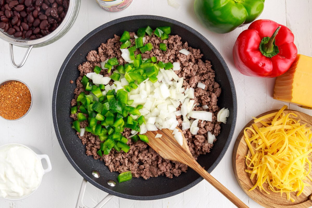 diced onion and bell pepper over ground beef in a pan