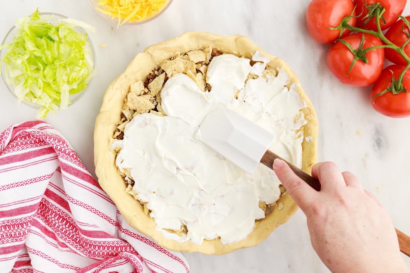 spatula spreading sour cream over taco pie