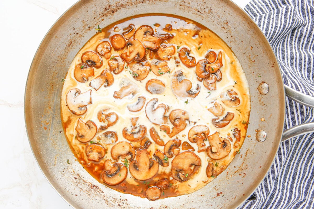 heavy cream and wine added to mushrooms in a skillet