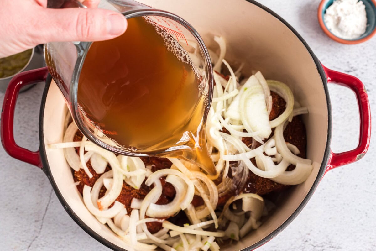 pouring broth into dutch oven with onions and chuck roast