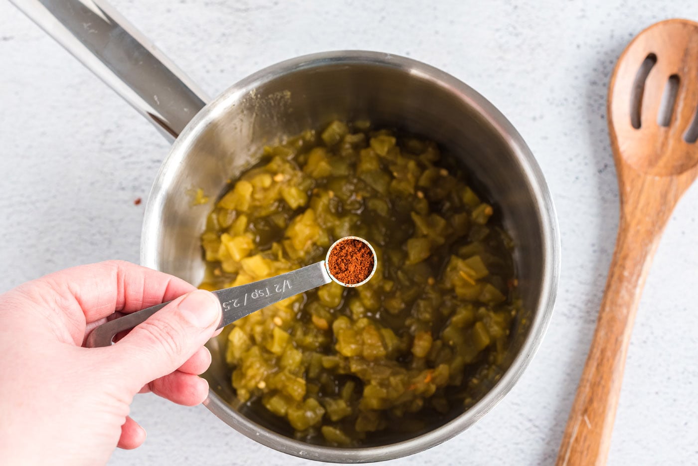 adding chile powder to green chiles in a saucepan