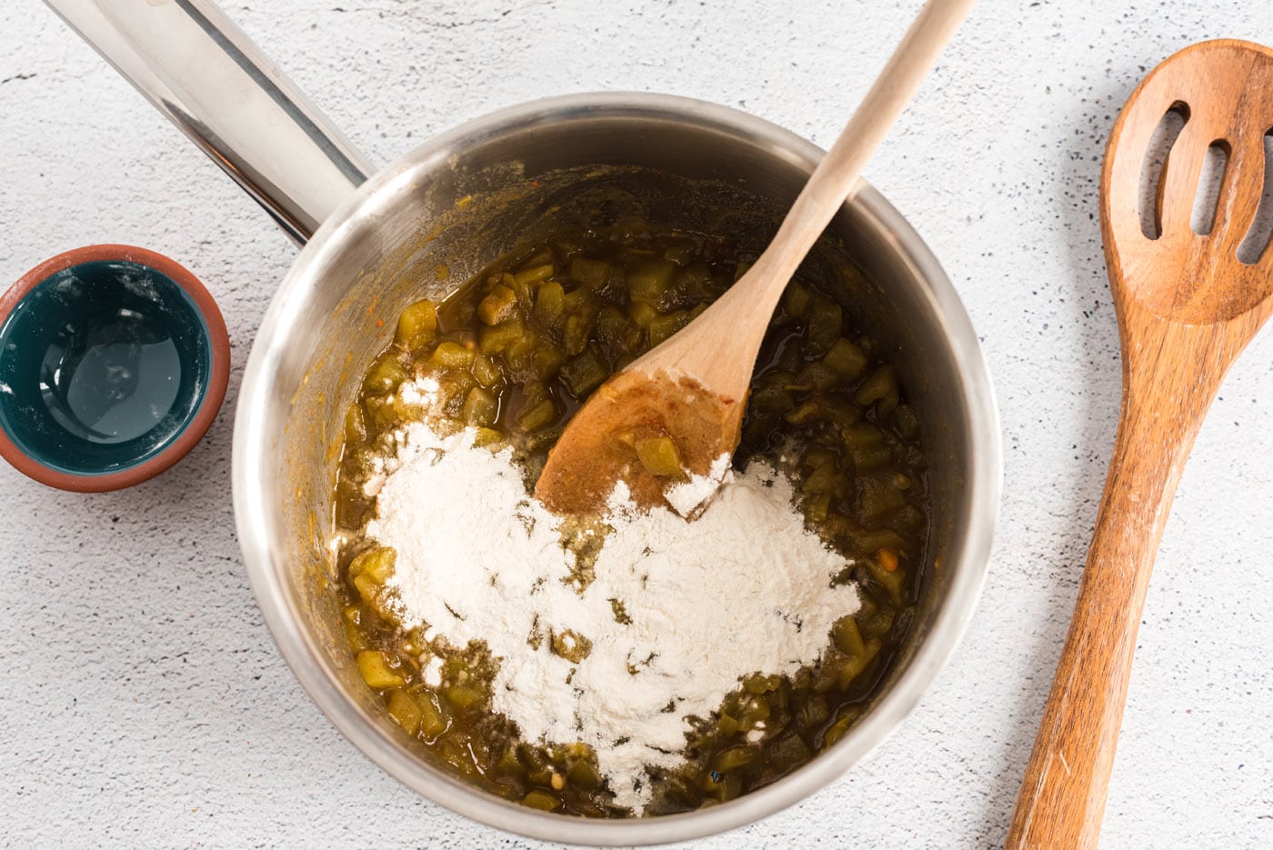 adding flour to green chiles in a saucepan