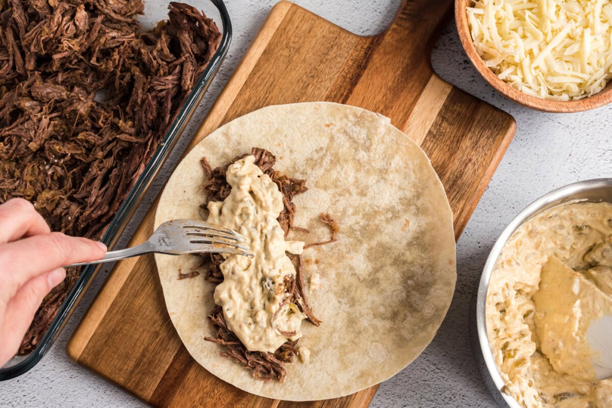 adding sour cream mixture to shredded beef enchiladas