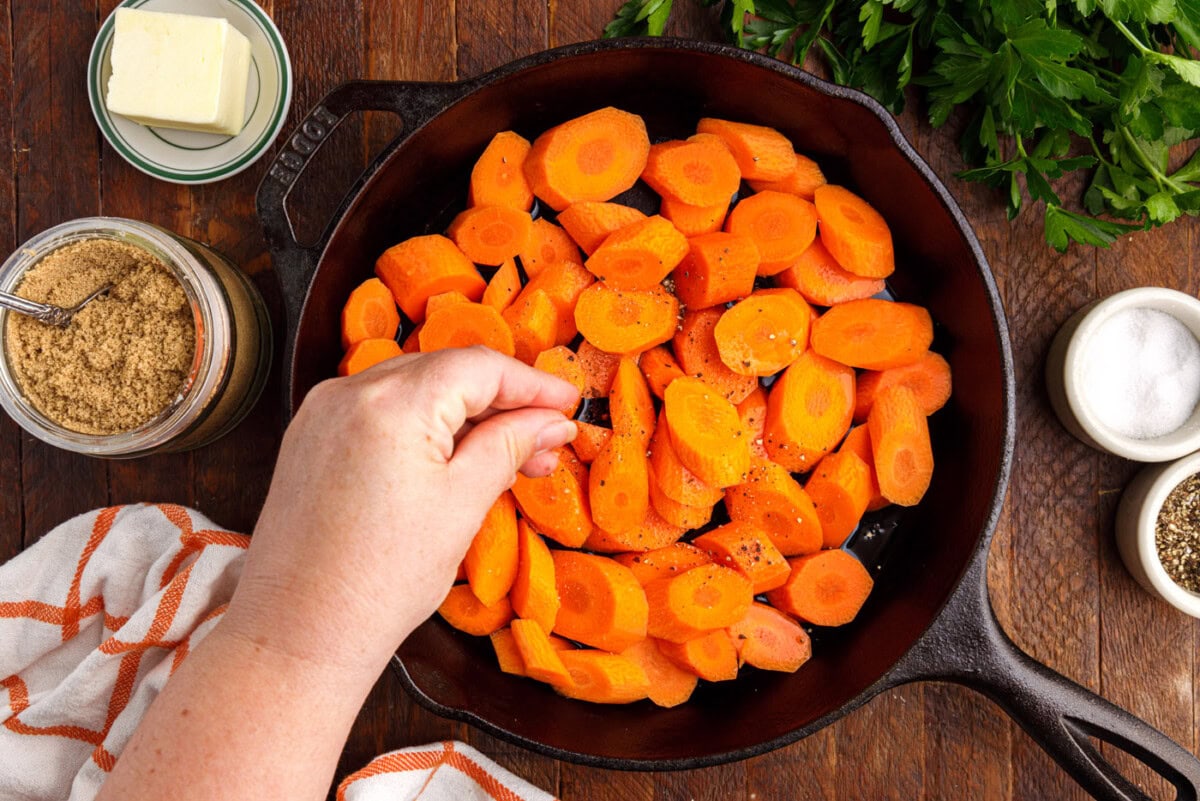 adding salt and pepper to skillet with sliced carrots
