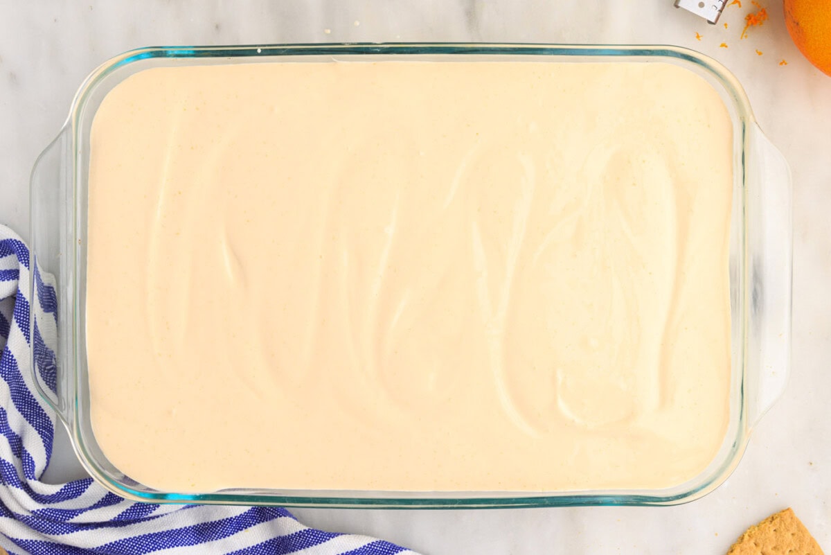 orange pudding mixture over graham crackers in a casserole dish