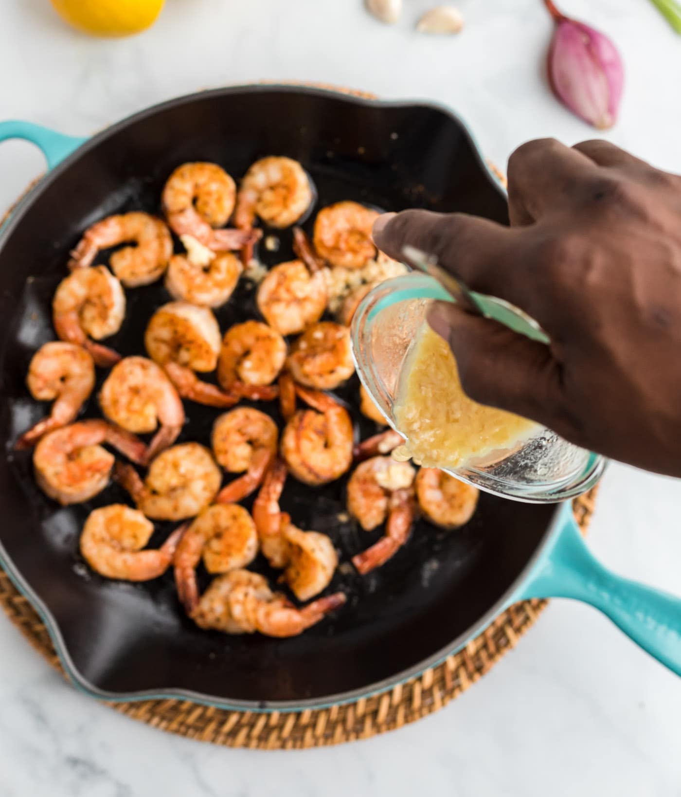 pouring butter sauce into skillet of sauteed shrimp