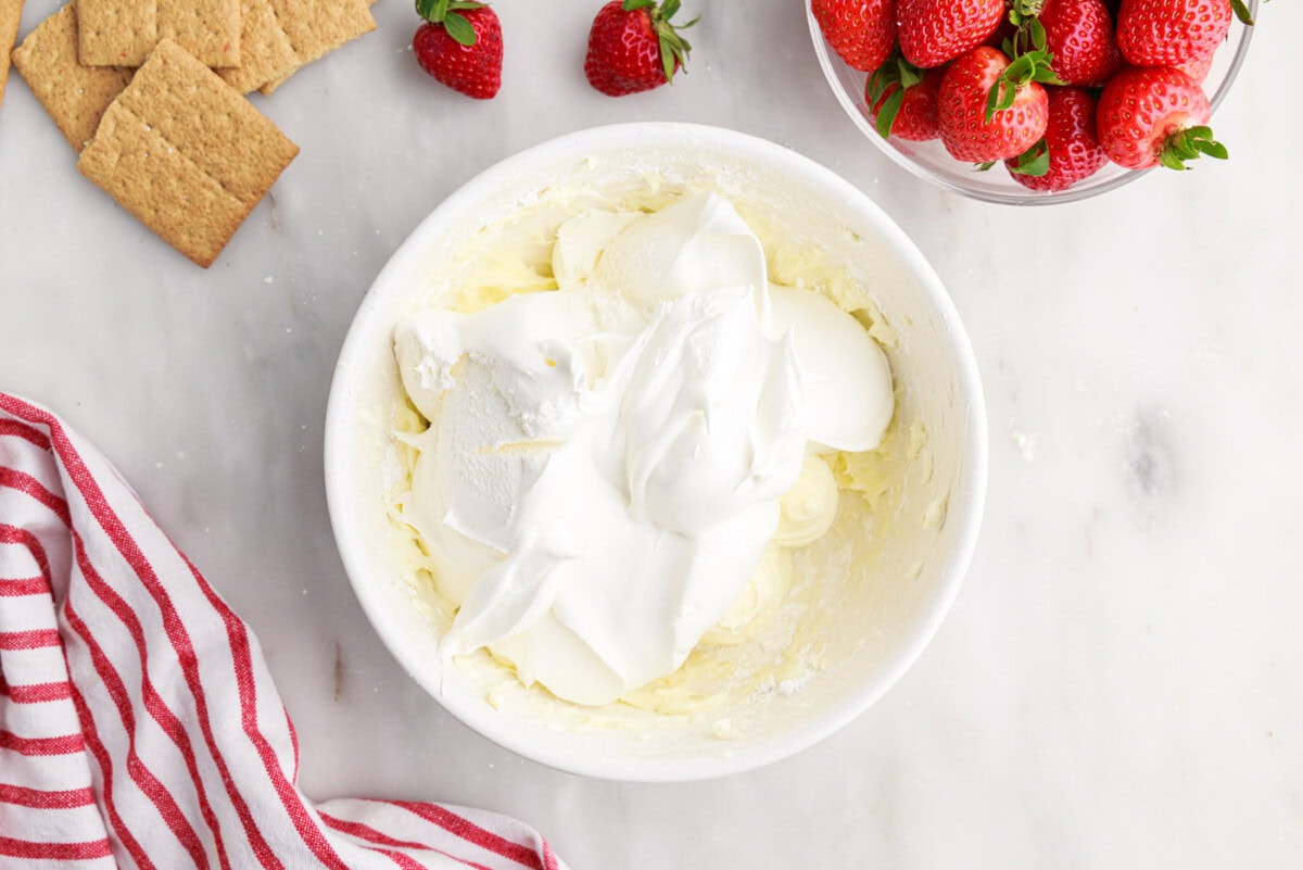 cool whip on top of cheesecake mixture in a bowl