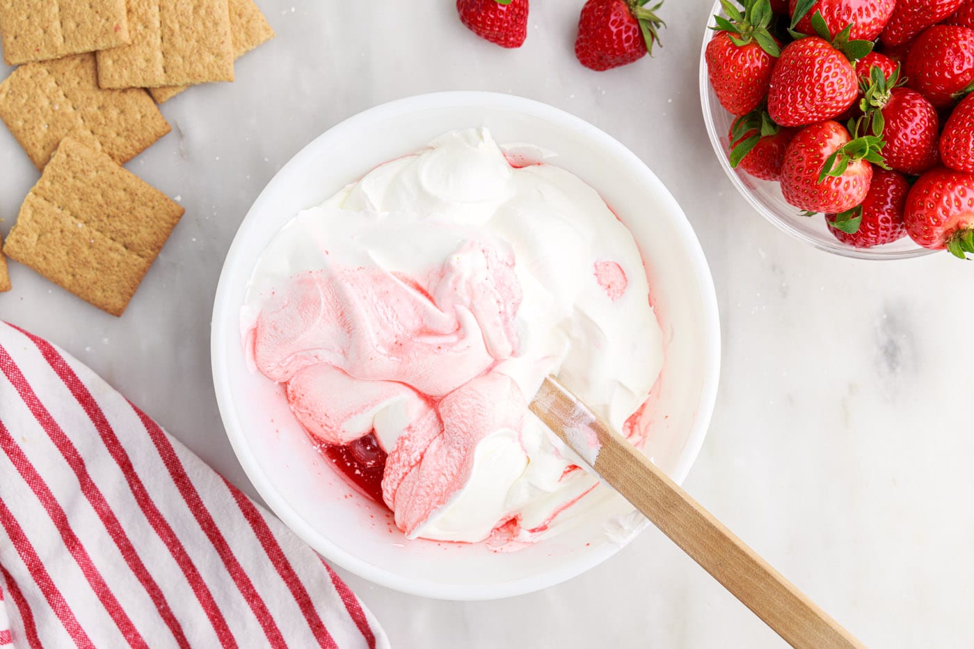 wooden spoon folding whipped topping into strawberry mixture