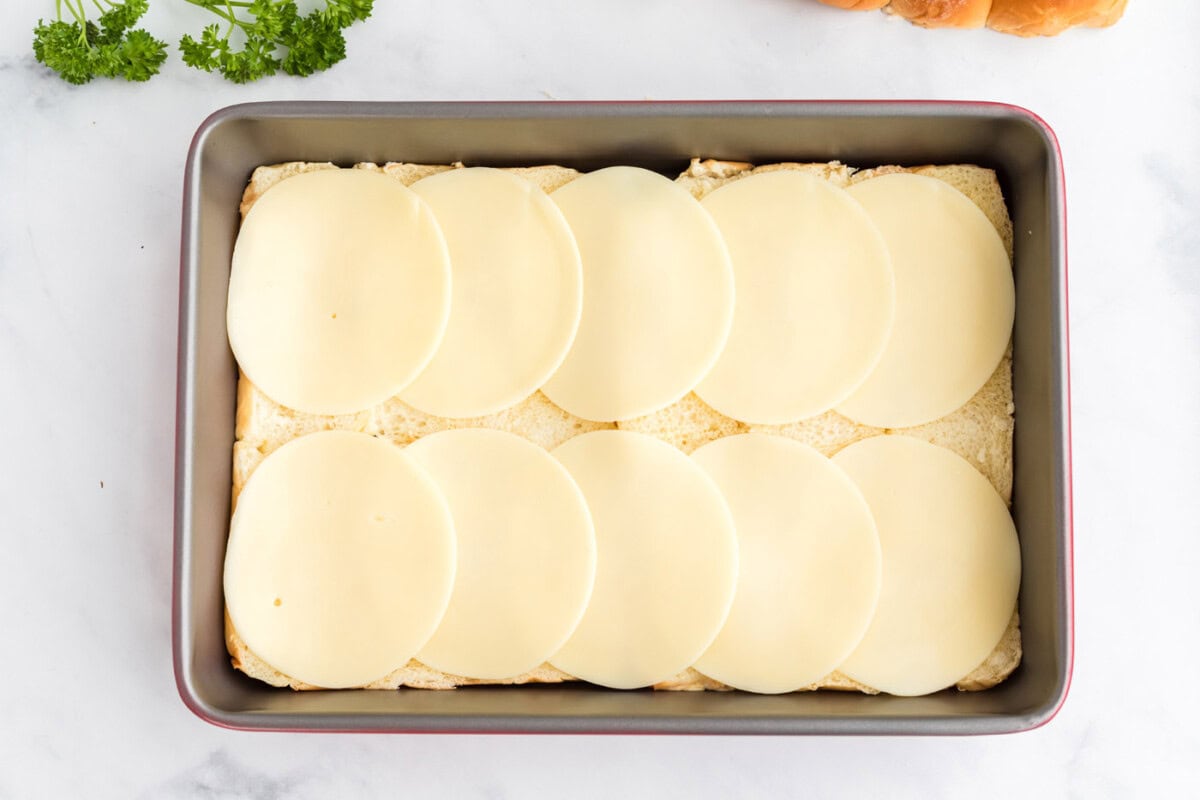 provolone cheese on top of hawaiian rolls in a pan