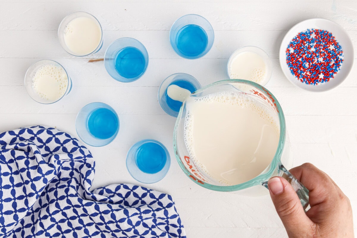 pouring sweetened condensed milk jelly on top of blue jello
