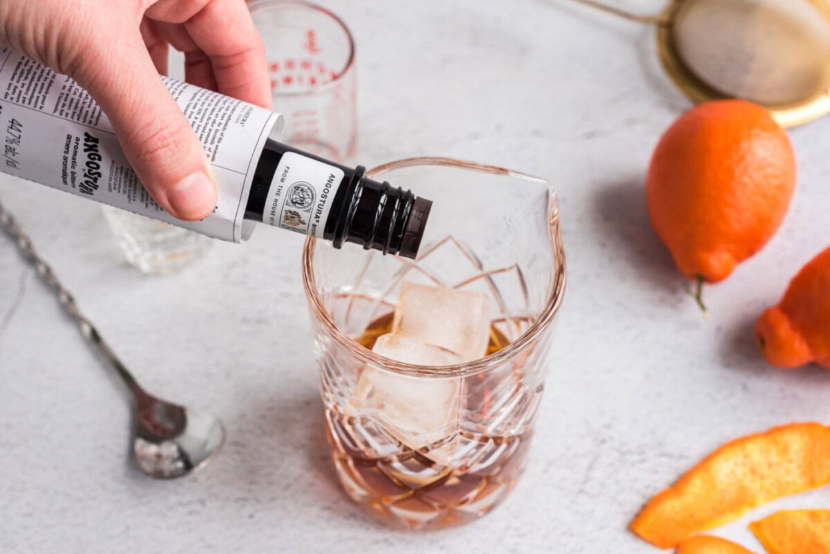 adding bitters to manhattan cocktail mixing glass