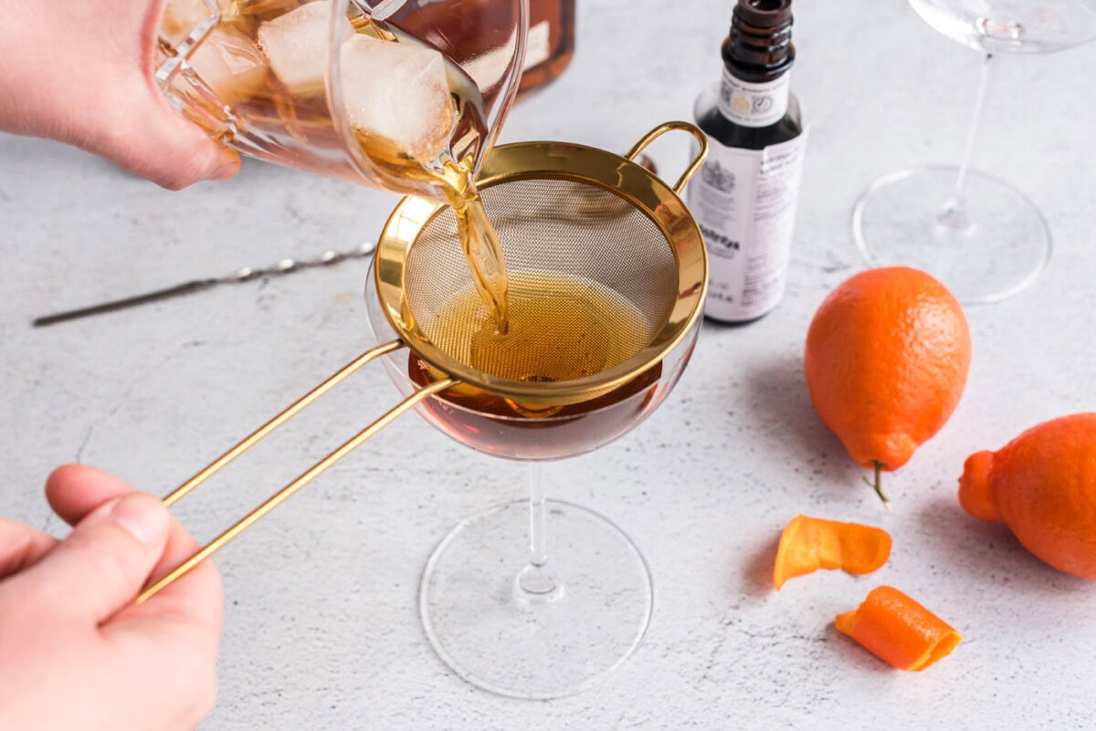 straining manhattan cocktail into a coupe glass